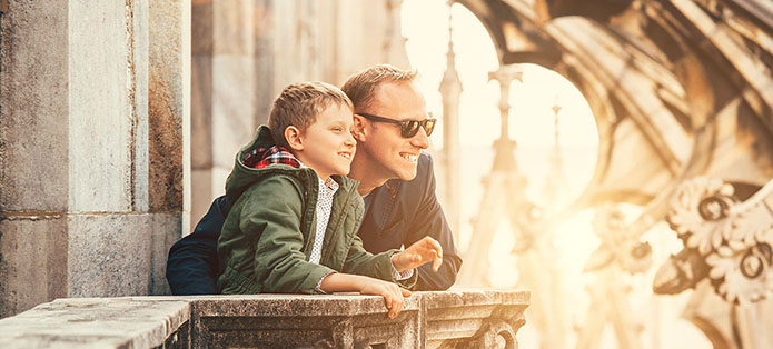 A father and son smiling together overlooking a city from a balcony.