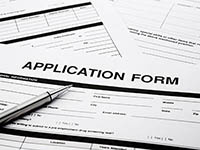 Application forms on a table with a pen resting on top