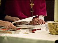 A priest signs documents with another person standing nearby